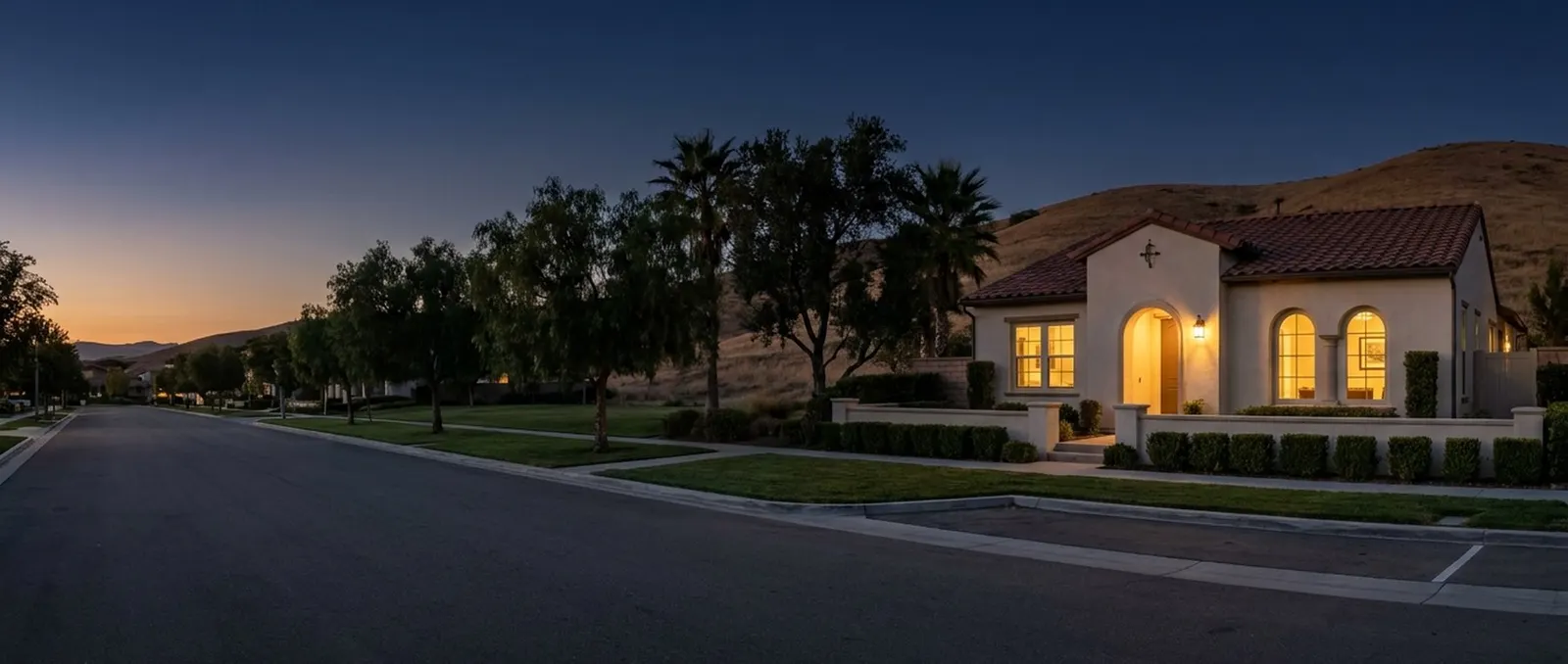 A model home at dusk with its lights on, the street empty.